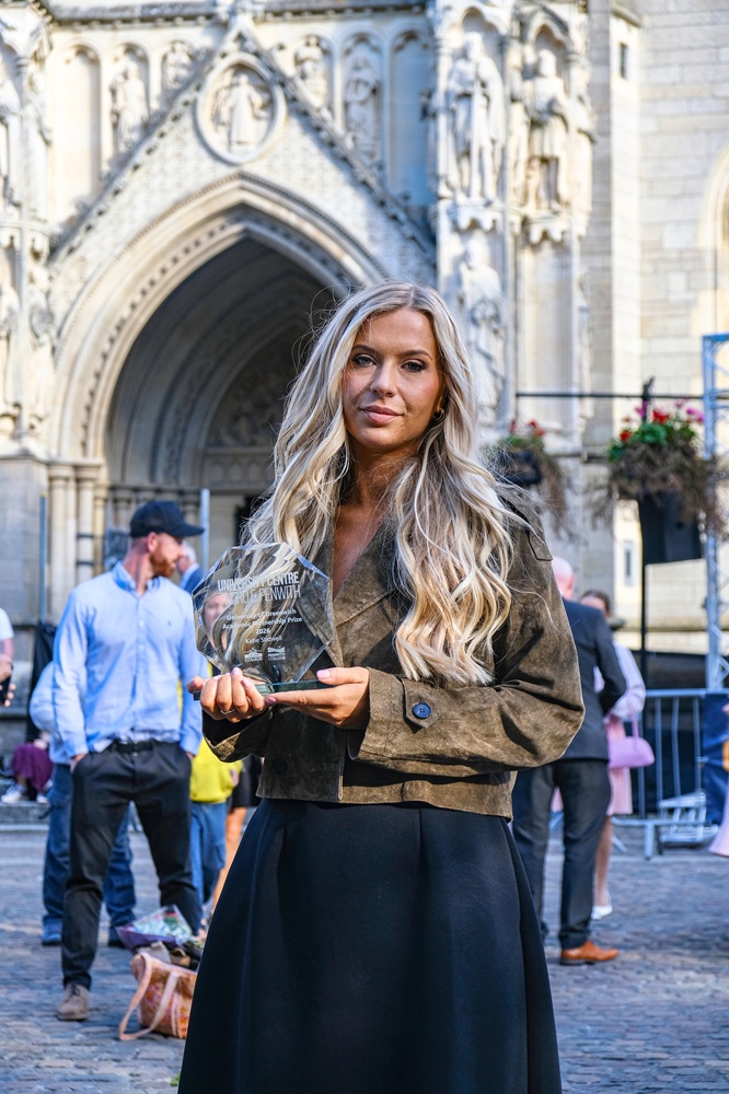 A student holding a glass trophy outside of the Truro cathedral.