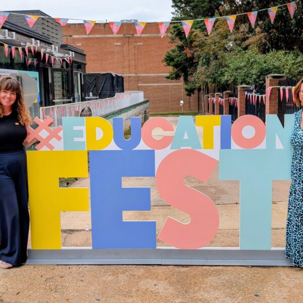 Two members of staff stood by a sign that says #EducationFest.