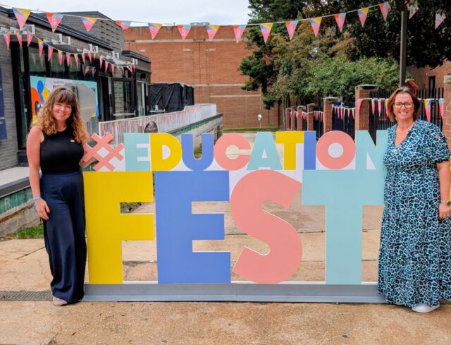 Two members of staff stood by a sign that says #EducationFest.