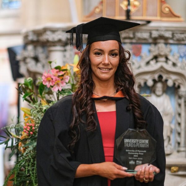 Sam Elson-Jones in graduation robes holding a glass trophy.