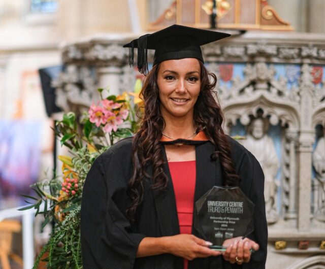 Sam Elson-Jones in graduation robes holding a glass trophy.