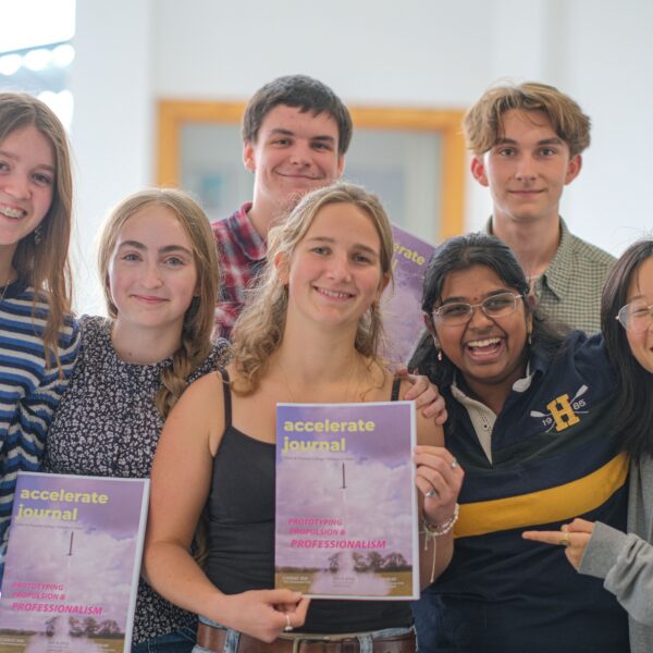 7 students stand, smiling, holding a magazine