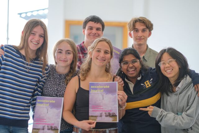 7 students stand, smiling, holding a magazine