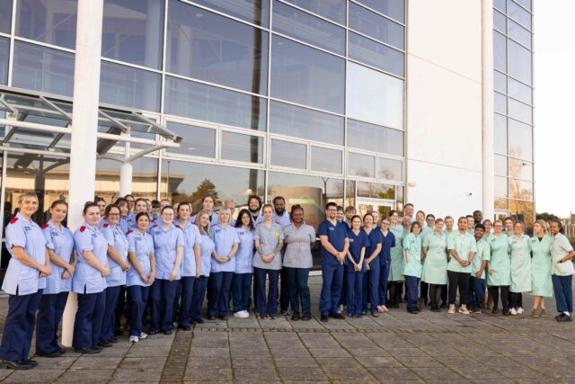 Large group of student nurses, in uniform, stood outside.