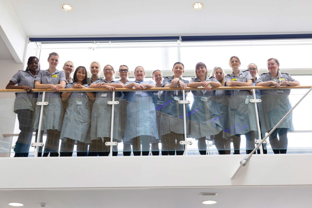 Group of student nurses, stood on balcony, looking down at camera smiling