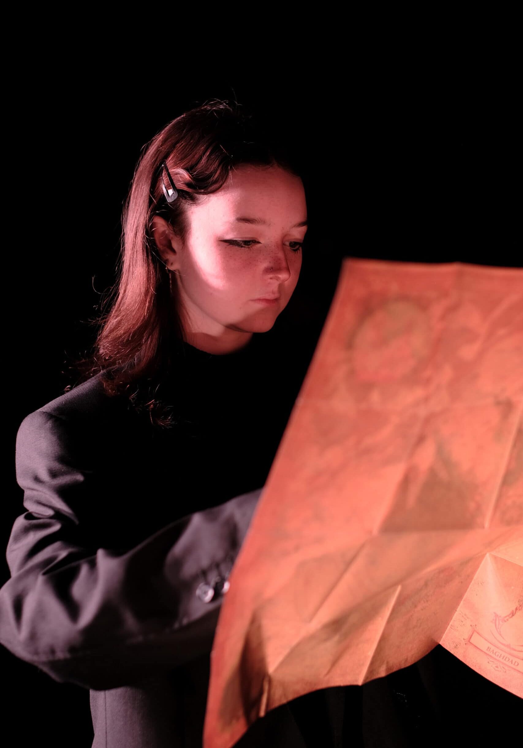 Jaime Level 3 Diploma in Performing Arts Theatre at Truro and Penwith College. Jaime is looking at a large map and wearing a dark suit with dramatic lighting.